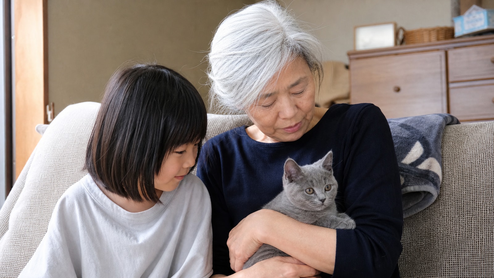 白髪の女性と子どもが並んで座り、腕の中の子猫を一緒に覗き込んでいる様子