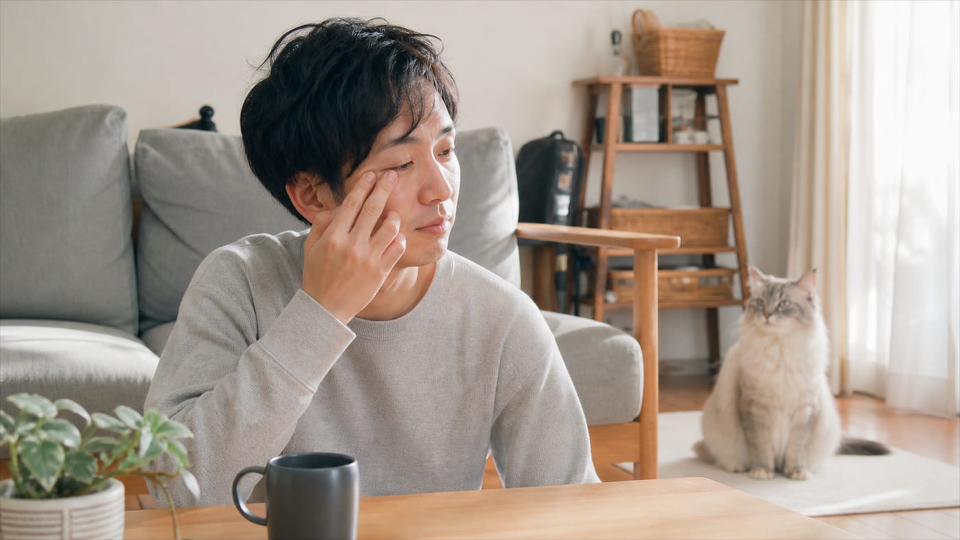 目のかゆみを感じて目元を押さえる人と、そばにいる猫